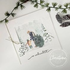 a christmas card with pine cones and evergreens on the table next to it is an image of a couple walking in the woods