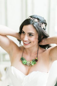 a woman in a white dress is smiling and wearing a necklace with flowers on it