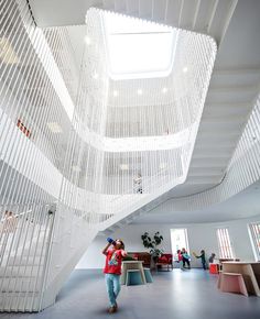 a woman is walking through an open space with white walls and ceiling lights hanging from the ceiling