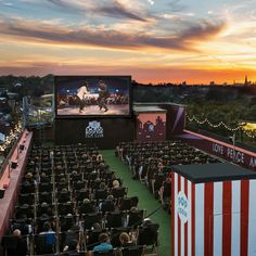 an outdoor movie theater at sunset with people sitting in chairs watching the movies on the screen