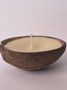 a white candle in a wooden bowl on a white surface with a stick sticking out of it