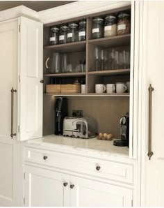 a kitchen with white cupboards filled with food and coffee machines on top of them