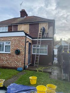 two men are painting the outside of a house with yellow buckets on the lawn