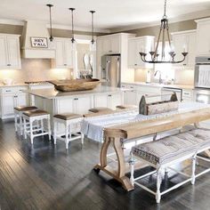 a large kitchen with white cabinets and wooden flooring, an island table surrounded by stools