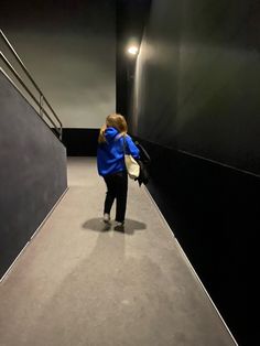 a young boy walking down a flight of stairs in an empty room with black walls