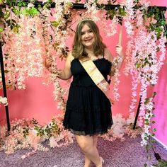 a woman in a black dress holding up a gold sash and posing for the camera