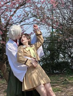 two people dressed in costume standing next to each other under a cherry blossom covered tree