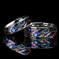 two rings that are sitting next to each other on a reflective surface with black background