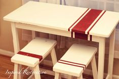 a white table with two stools and a red stripe on the top in front of a window