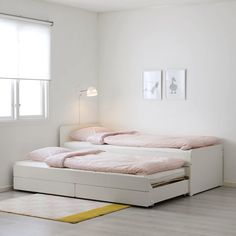 a white bed with pink sheets and pillows in a room next to a yellow rug