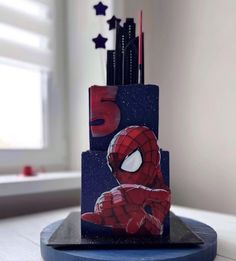 a three tiered cake with spiderman on it's side and stars in the background