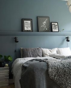 a bedroom with blue walls and two pictures on the wall above the bed, along with a gray blanket