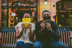 a man and woman sitting on a bench taking pictures with their cell phones in front of them