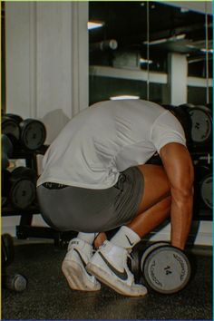 a man squatting down in front of a row of dumbbells