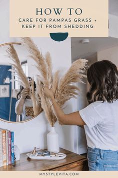 a woman standing in front of a mirror with pampas grass hanging on the wall