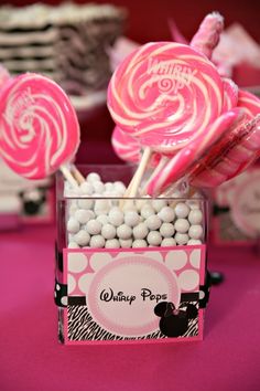 pink and white lollipops in a square container on a table with other candies