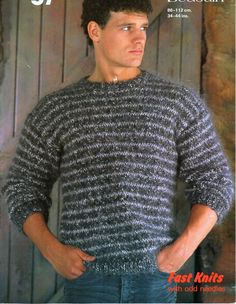 a man standing in front of a wooden wall with his hands on his hips wearing a sweater