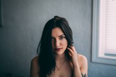 a woman with long dark hair is posing for the camera in front of a window