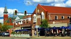 an old brick building on the corner of a street with people sitting at tables under umbrellas