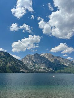 a lake with mountains in the background under a blue sky filled with white fluffy clouds