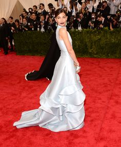 a woman in a white gown and black jacket walking on the red carpet with cameras