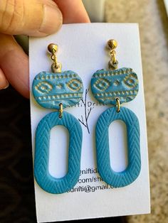 a pair of blue earrings is being held by a person's hand on a card