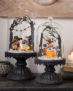 two snow globes with halloween decorations on them sitting on a table next to candles