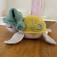 a crocheted turtle with a green hat on it's head sitting on a wooden table