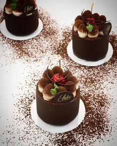 three chocolate desserts with cherries and toppings on white plated serving platters