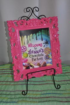 a welcome sign is displayed in a pink frame on a green and white striped blanket