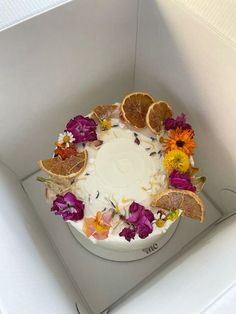 a white cake with orange slices and flowers on the top is in a cardboard box