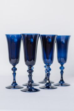 four blue glass goblets sitting side by side on a white surface, with one in the middle