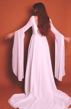 This is a stunning and rare 1960's fairytale renaissance vintage wedding dress - i have truly never seen one quite like this. it is a sleek white dress with two layers: a solid white underlay and a sheer white overlay. this zips closed in the back fitting the detailed beaded waist to your shape. the top of the dress is adorned with circle clusters of beads resembling a star or snowflake making this so lovely for a winter wedding. the true star is clearly the sleeves - they are long dramatic sheer draping sleeves that have very subtle flower clusters of sequins through out. this piece is in insane condition for age and does't show signs of wear. please note below for sizing and feel free to ask any questions you may have before purchasing.  brand bonny size 12 length front 60" length back 9 Elegant White Medieval Dress For Costume Party, Medieval White Dress For Costume Party, White Fitted Ethereal Dress, Medieval Style White Wedding Dress, Elegant White Medieval Wedding Dress, Medieval White Dress With Fitted Bodice, Vintage Floor-length Medieval Wedding Dress, White Long Sleeve Costume Gown, Elegant White Wedding Dress For Costume