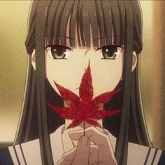 a girl with long black hair holding a red leaf in front of her face and looking at the camera