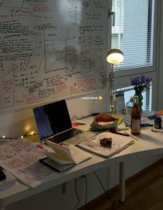 a laptop computer sitting on top of a desk next to a window covered in writing