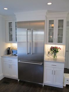 a kitchen with white cabinets and stainless steel refrigerator freezer combo in the center, surrounded by wood flooring