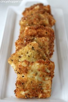 three pieces of fried food on a white plate with parmesan cheese and seasoning