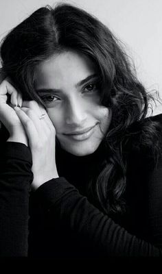 a black and white photo of a woman with her hands on her head, smiling