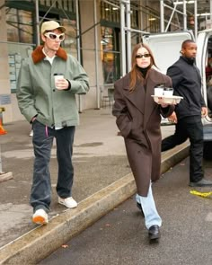 the woman is walking down the street with her coffee in hand and another man standing next to her