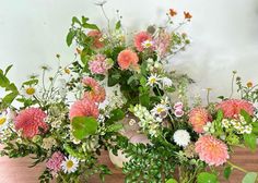 a vase filled with pink and white flowers on top of a wooden table next to greenery