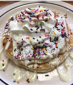 a white plate topped with pancakes covered in whipped cream and sprinkles,