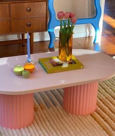 a pink table with flowers in a vase on it and a book sitting on top