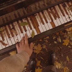 a person standing in front of an old piano with autumn leaves on the ground next to it