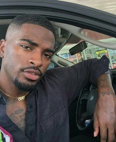 a man sitting in the driver's seat of a car with tattoos on his arm