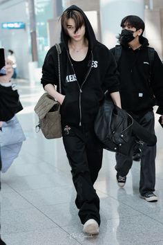 two people walking through an airport wearing black sweatshirts and masks on their faces as they carry luggage