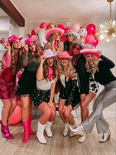 a group of women posing for a photo with pink hats and balloons on the wall behind them