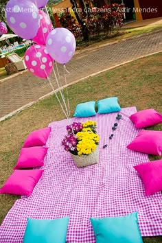 a table with pink and blue pillows on it, some yellow and purple balloons in the background