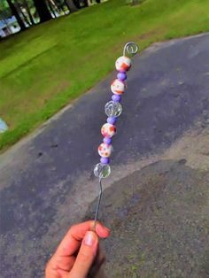 a person is holding a glass bead necklace on a stick in the street with grass and trees in the background