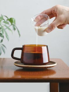 a person pouring milk into a coffee cup