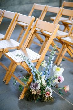 several wooden chairs with flowers on them sitting side by side in the middle of an aisle